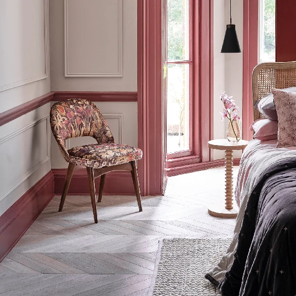 Bedroom with pink skirting and floral upholstered chair.