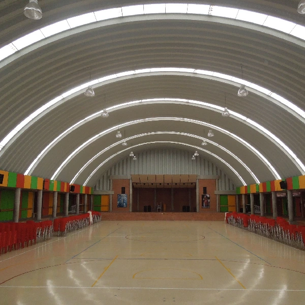 Gymnasium with arched roof, stage, and wood sports floor.