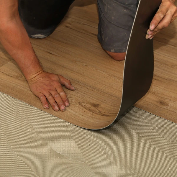 worker installing flexible wood-effect vinyl click flooring over a subfloor.